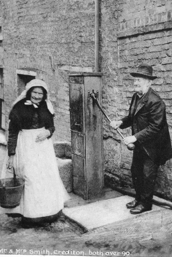 Photograph of a man and a woman drawing water from an old pump